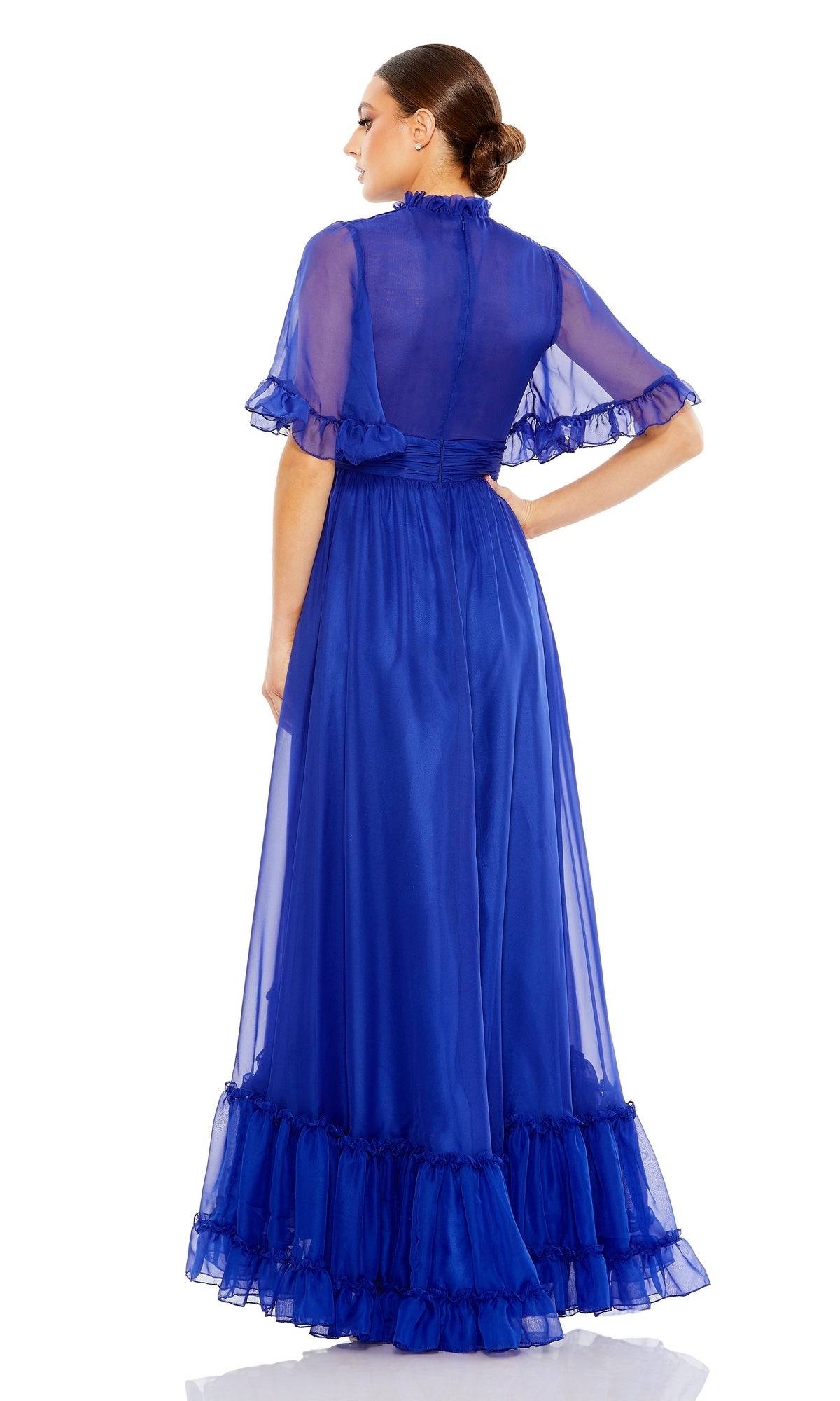 A woman faces away, wearing the Mac Duggal 68229—a royal blue sheer long formal dress with short ruffled sleeves and hem—standing against a white background.